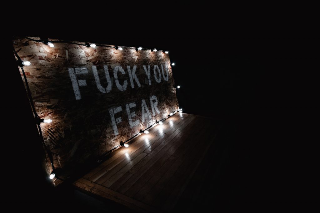 Lighted particle board with the white stenciled letters "Fuck You Fear" in the darkness